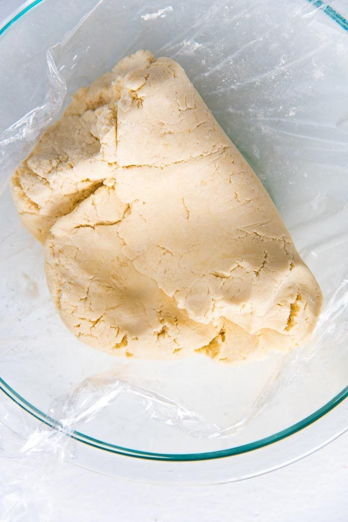 The shortbread dough in a plastic lined glass bowl, being folded over to bring together to form a dough ball.
