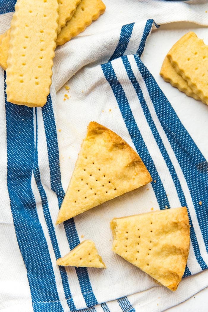 An overhead view of baked scottish shortbread cookies and classic shortbread cookies on a blue and white striped tea towel.