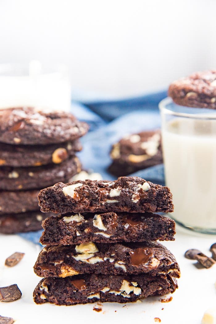 A stack of Triple Chocolate Chip Cookies, broken in half on a white table top. 