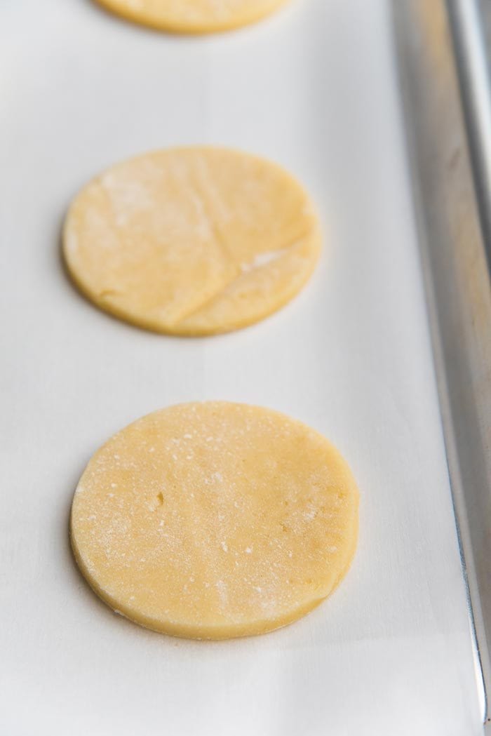 Cut and chilled round sugar cookies placed on a parchment paper lined baking tray ready to be baked.