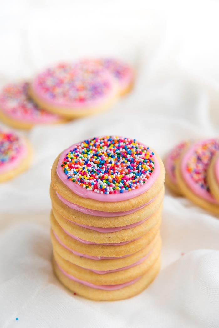 A stack of funfetti cookies with pink sugar cookie frosting and rainbow nonpareils. 