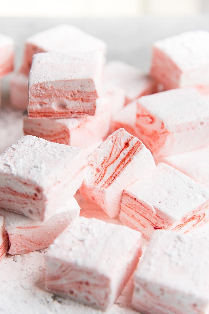 Freshly cut Peppermint marshmallows with red and white swirls, on a cutting board with mallow dusting powder.
