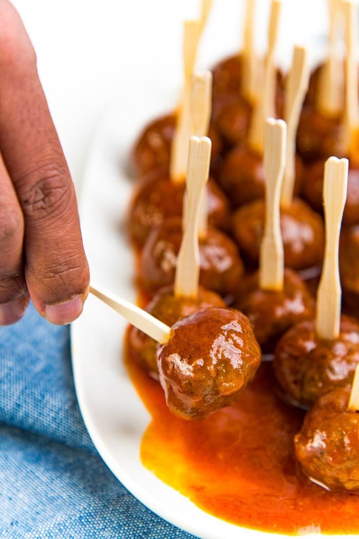 A cocktail meatball being picked up from the white serving platter, coated with a sweet and spicy sauce.