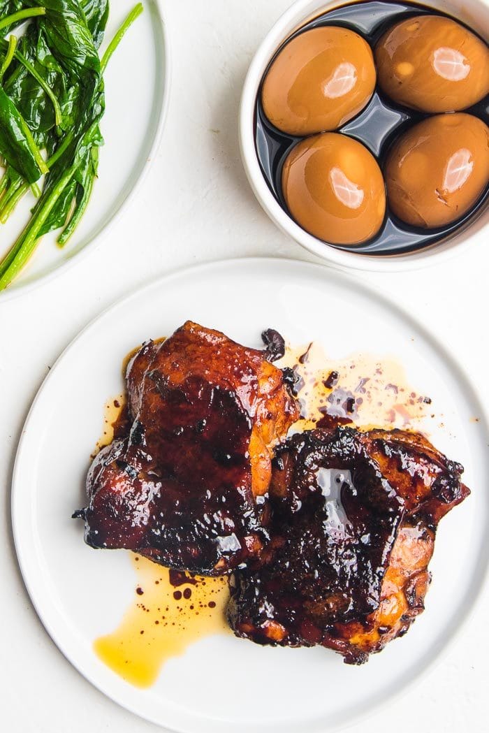 Two pieces of caramelized soy chicken made with chicken thigh pieces, on a white plate before being sliced.