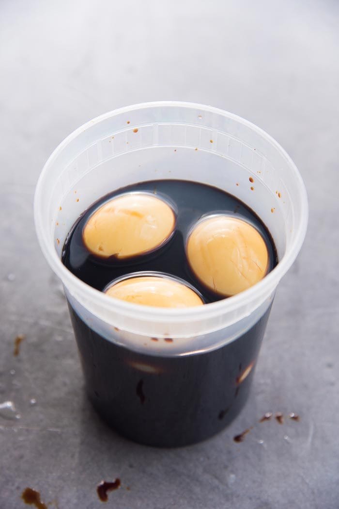 Soft boiled eggs placed in a container with the soy sauce mirin marinade to make ajitsuke tamago.