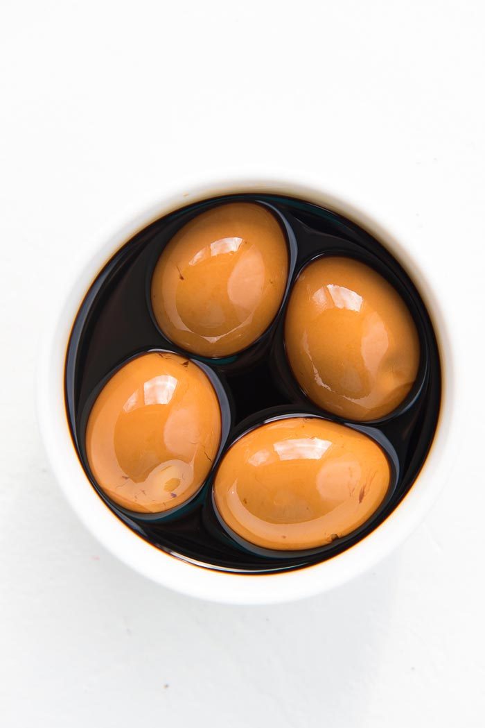 Marinated soft boiled eggs placed in a white bowl with the marinade - ready to be served. 