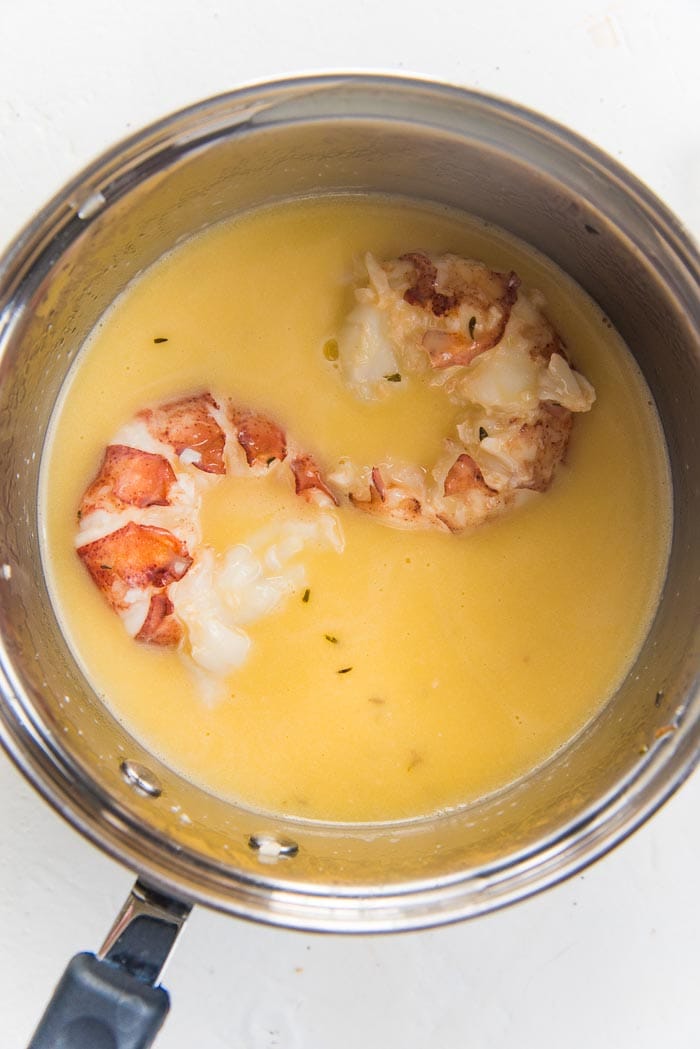 Lobster tails being poached in butter, in a small saucepan.