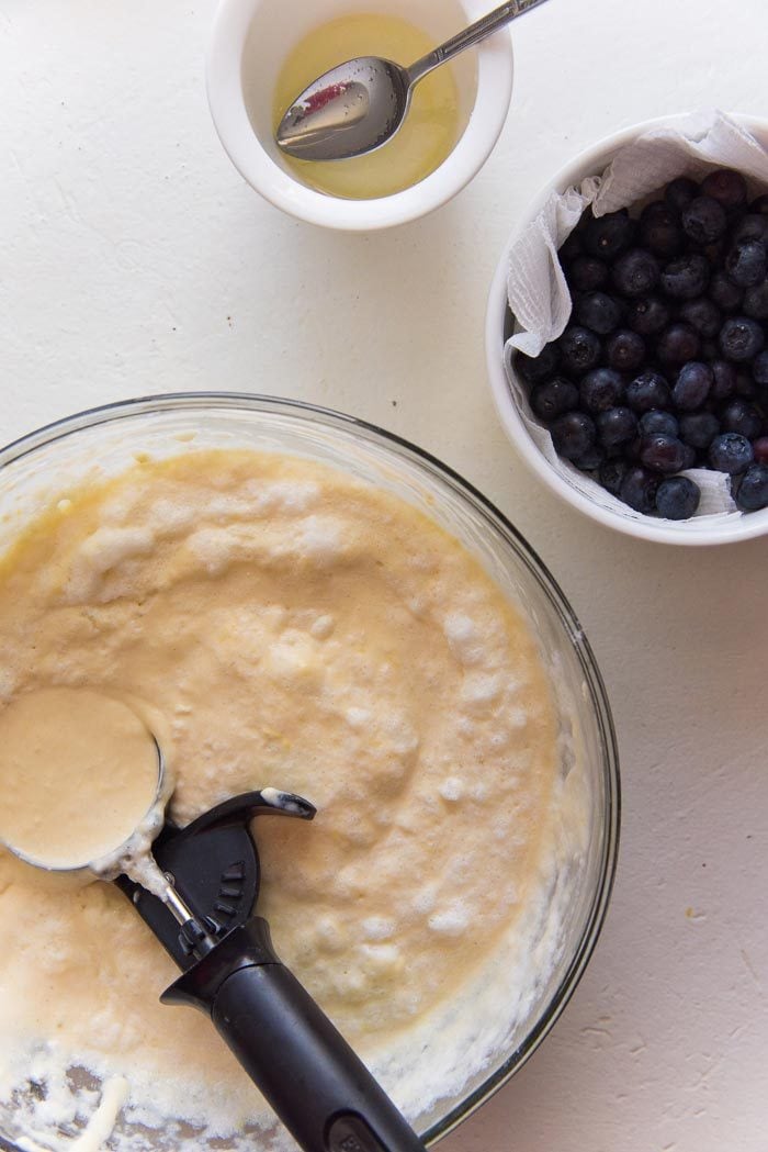 An overhead view of the pancake batter, melted butter and blueberries in separate bowls. 