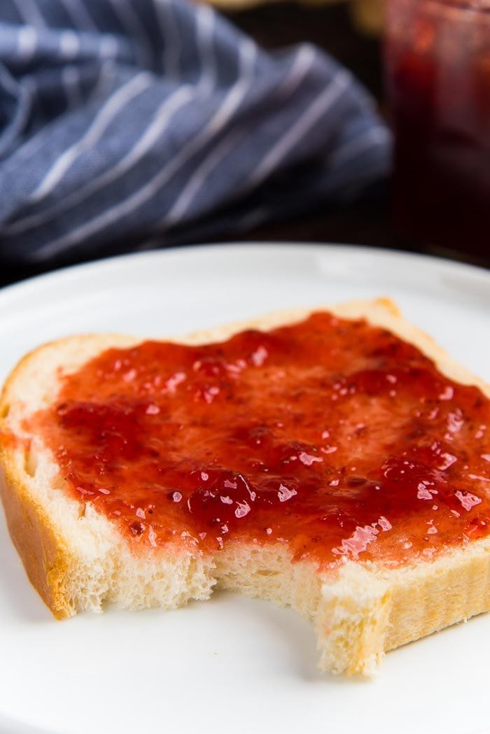 A close up of the slice of homemade white bread with jam spread on top, with a bite taken out.