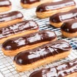 Eclairs with pastry cream and chocolate glaze resting on a wire rack. 