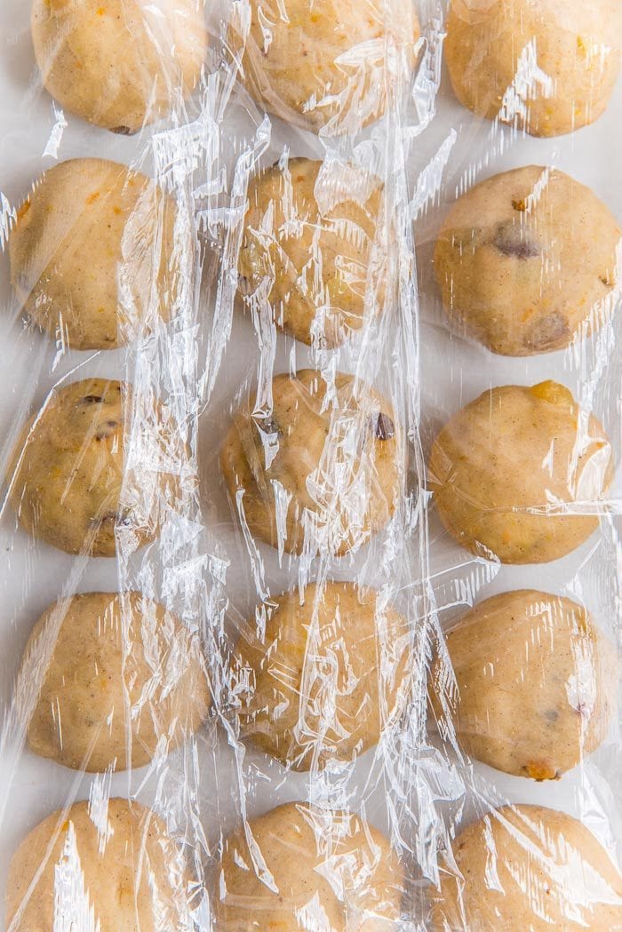 Individual hot cross buns, shaped into smooth balls and placed on top of a parchment lined baking tray, and covered with plastic wrap, for proofing.