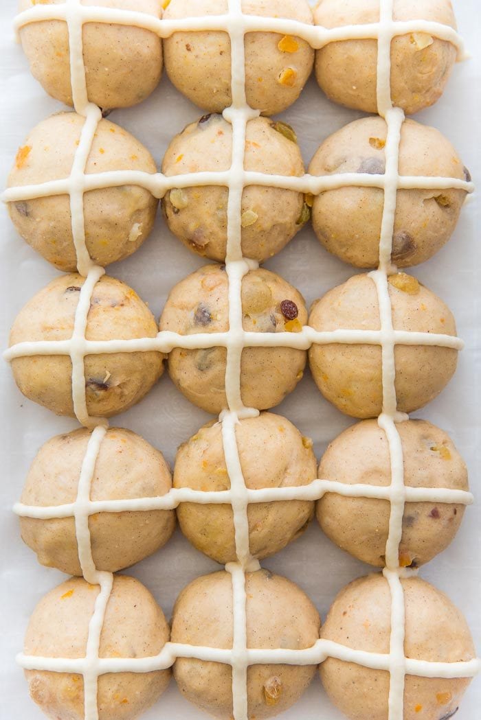 Proofed classic hot cross buns, with flour crosses on top, ready to be baked.