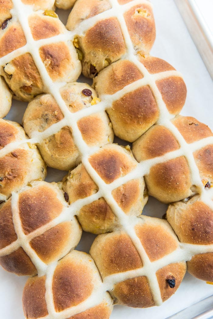 Freshly baked soft hot cross buns, cooling own on a lined baking tray. The hot cross buns have not been glazed yet.