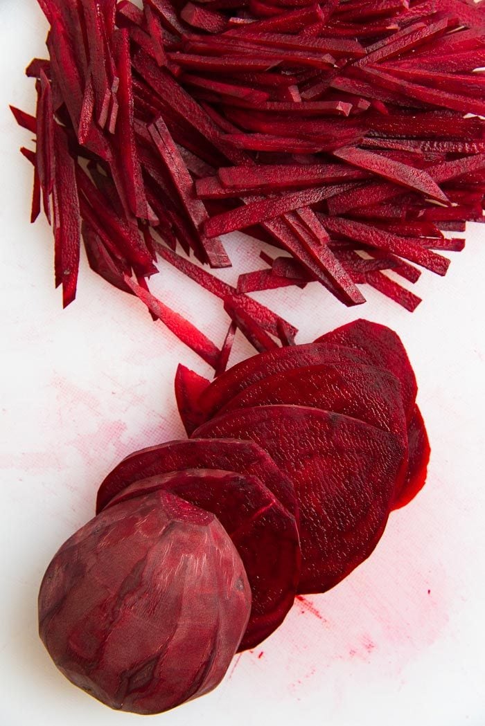 Raw beetroot peeled, sliced and julienned on a white cutting board.