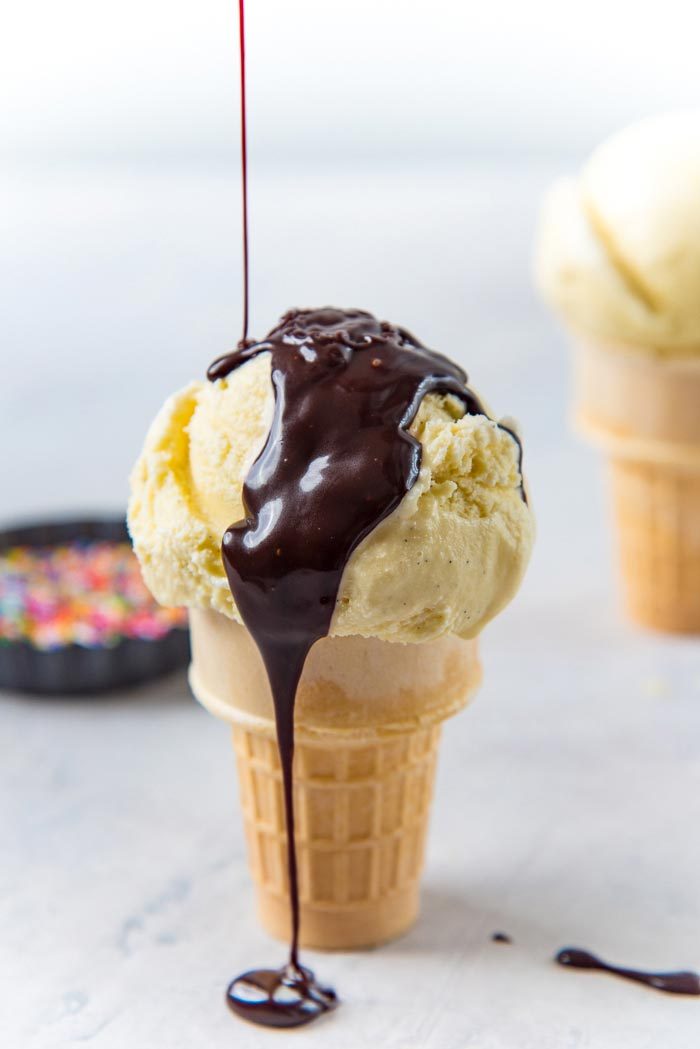 Chocolate fudge sauce being poured on top of a vanilla ice cream cone.