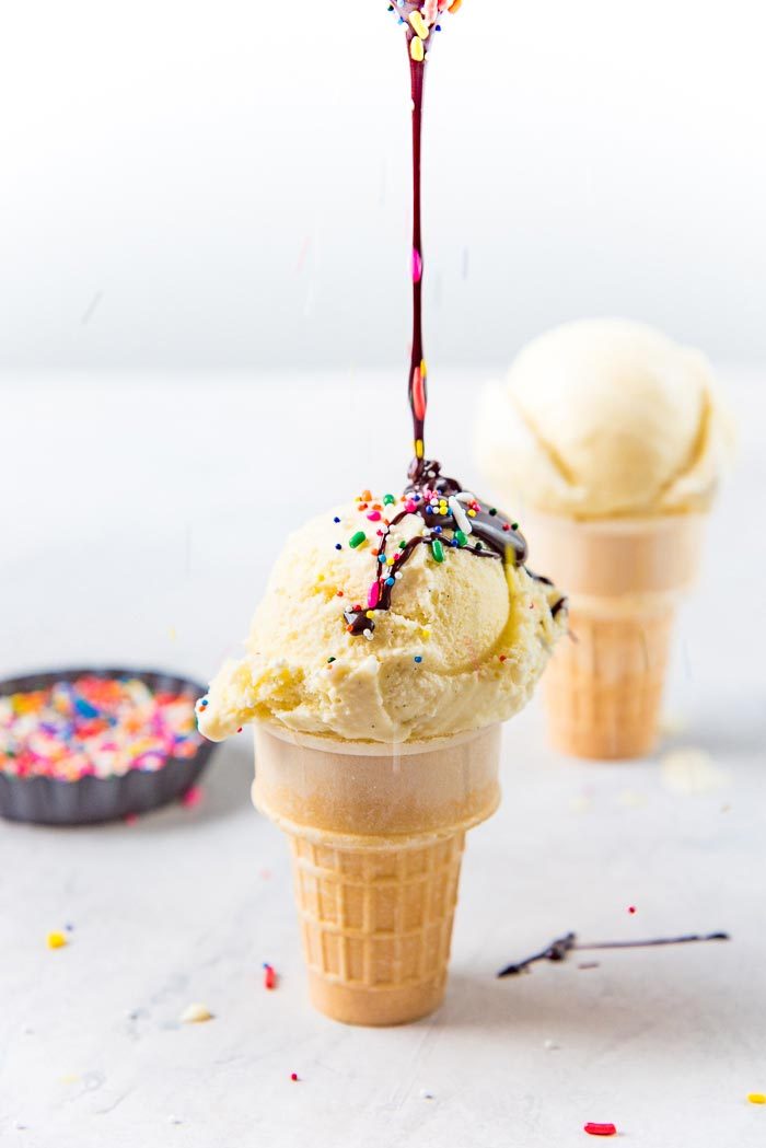 An ice cream cone on a white table, with classic vanilla ice cream scoop on top, with chocolate sauce and sprinkles.