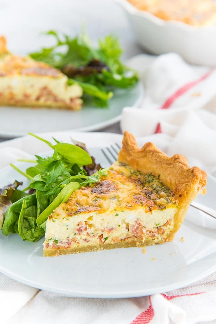 A slice of quiche lorraine on a light grey plate with a side salad
