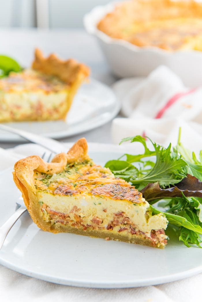 A slice of quiche lorraine, with a golden crust places on a plate with a side salad