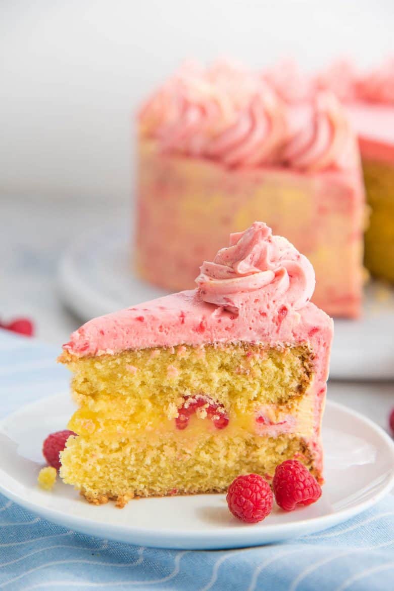 A slice of the lemon cake with lemon curd and raspberry frosting on a white plate
