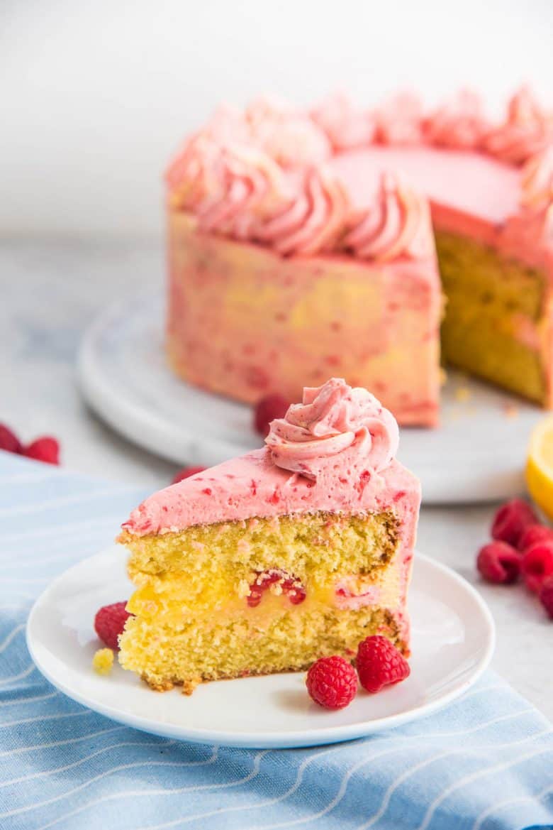 The whole lemon raspberry cake in the background, and slice of the lemon cake in the foreground