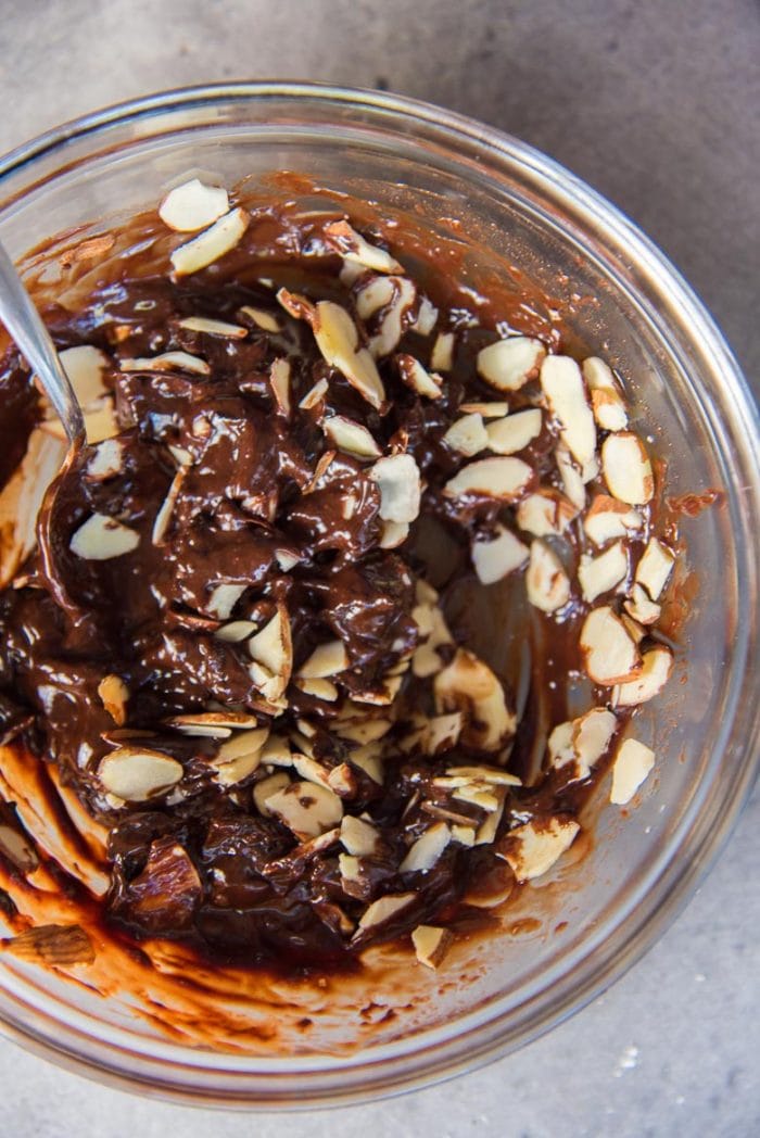 Melted chocolate and prunes being mixed with almonds
