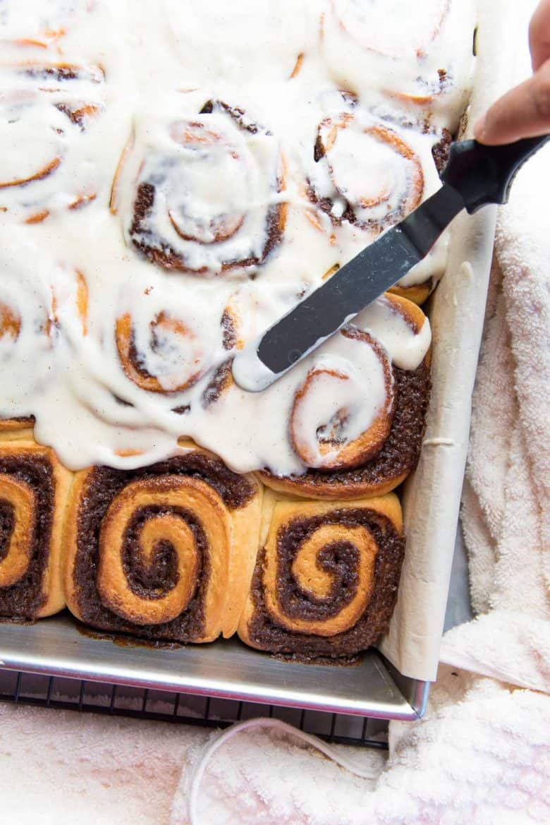 Cream cheese frosting being spread on the hot cinnamon rolls