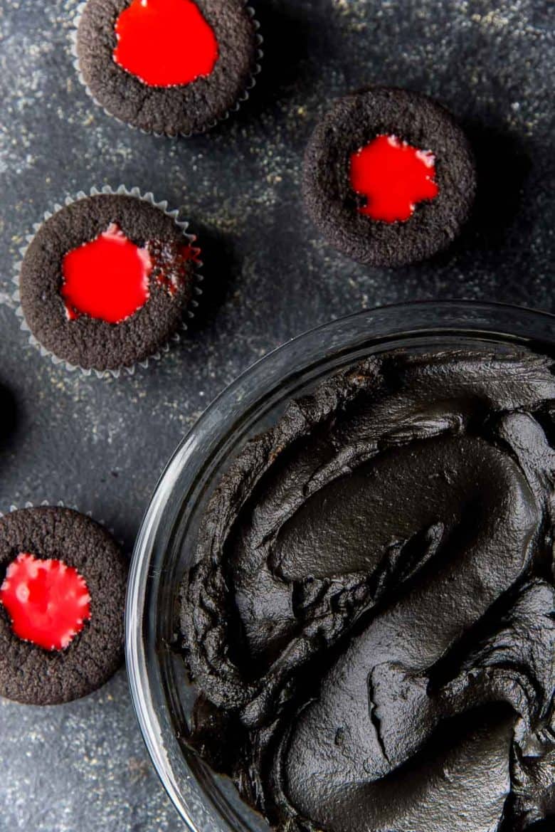 Red white chocolate ganache filling inside cupcakes with a bowl of black frosting