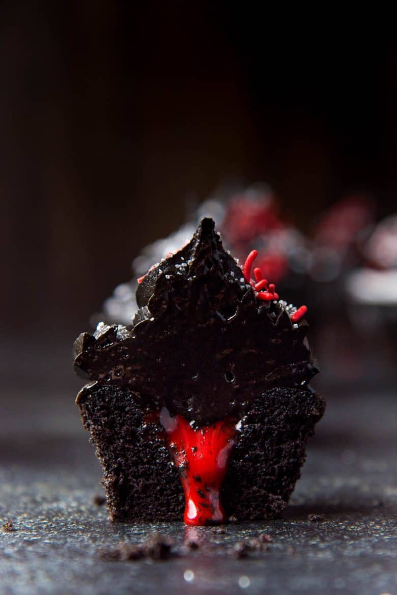 Bleeding Halloween black cupcake with black frosting cut in half with "bleeding" white chocolate ganache center