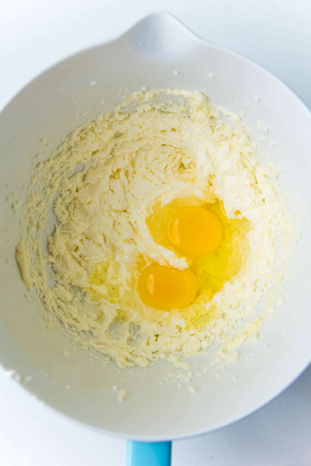 Adding eggs into the creamed butter and sugar mixture in the mixer bowl.