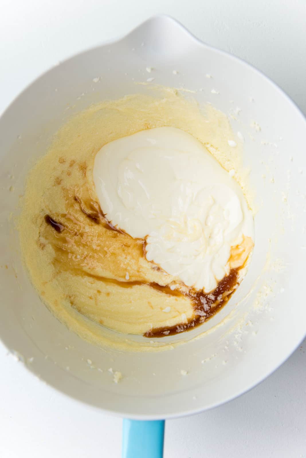 Adding sour cream and vanilla extract to the vanilla cupcake batter in the mixer bowl.