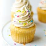 Moist, fluffy vanilla cupcake with a tall swirl of buttercream frosting and colorful sprinkles.