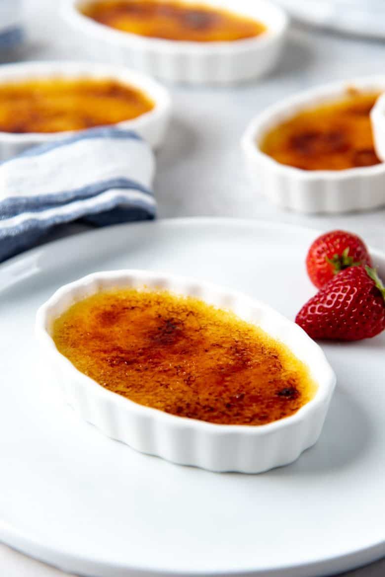 Ready to serve creme brulee placed on a white plate with a strawberry garnish