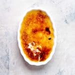 Oval dish with classic crème brûlée, where the caramelized top is broken in one spot to reveal creamy custard underneath.