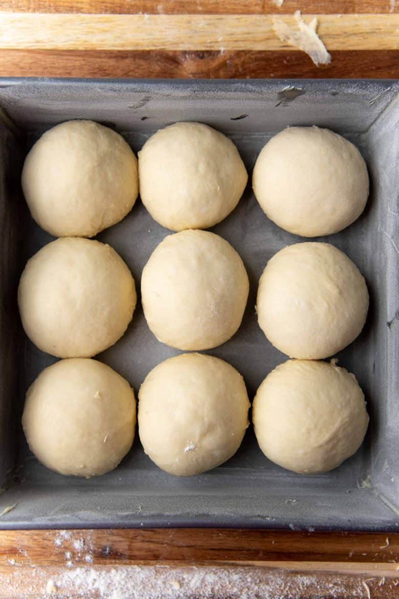 Nine bread rolls in a square pan ready to be proofed.