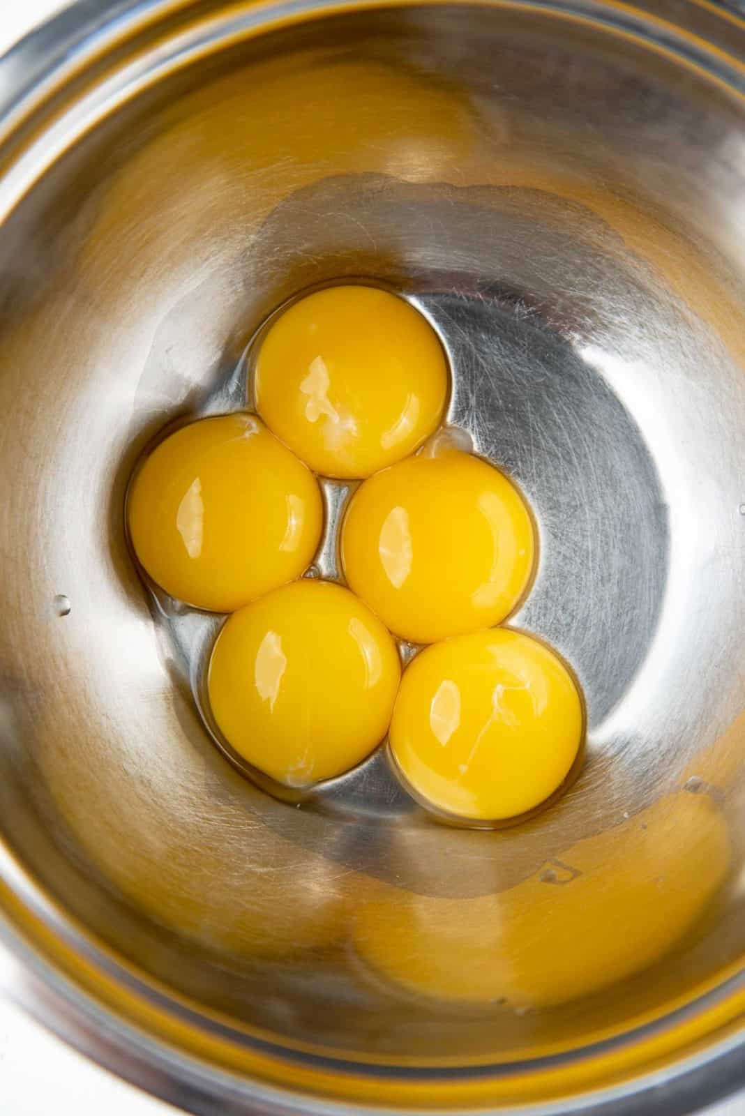 Five egg yolks in a metal bowl.