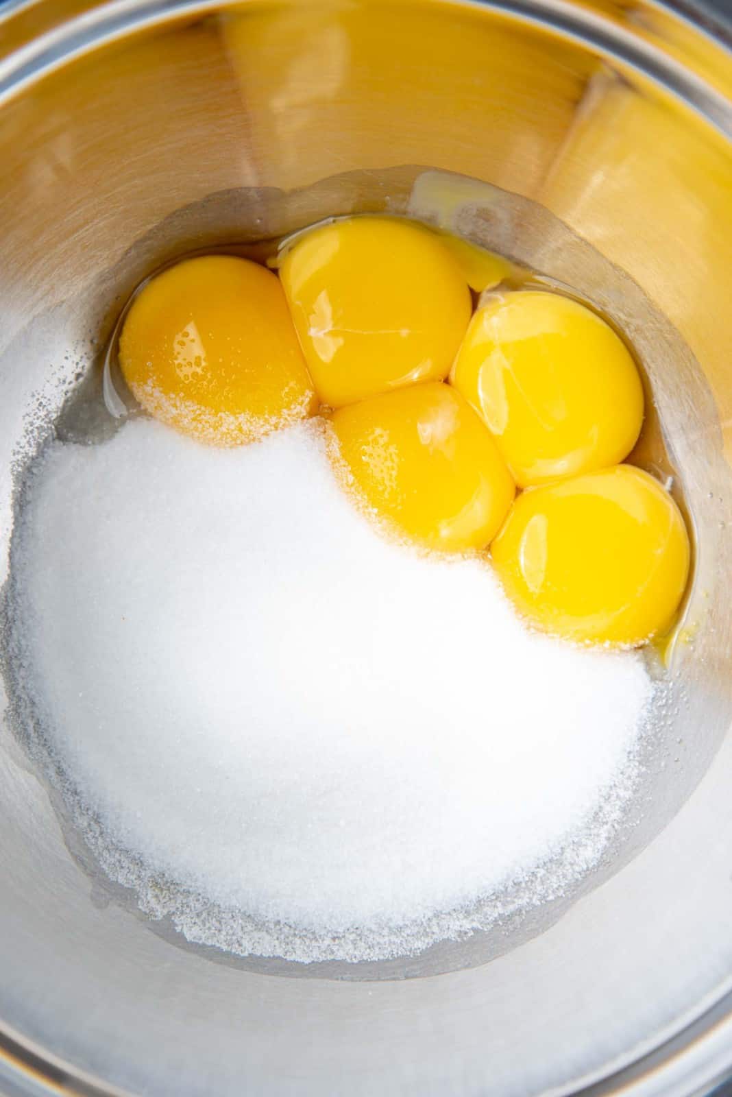 A metal bowl containing vibrantly yellow egg yolks and sugar, ready for mixing.