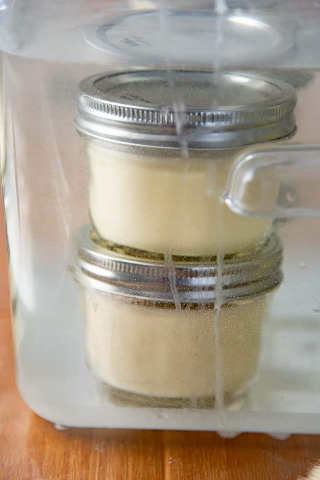 Two small jars filled with creme brulee custard cooking inside the sous vide circulator container.