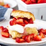Strawberry shortcake served with whipped cream and sliced fresh strawberries on a white plate.