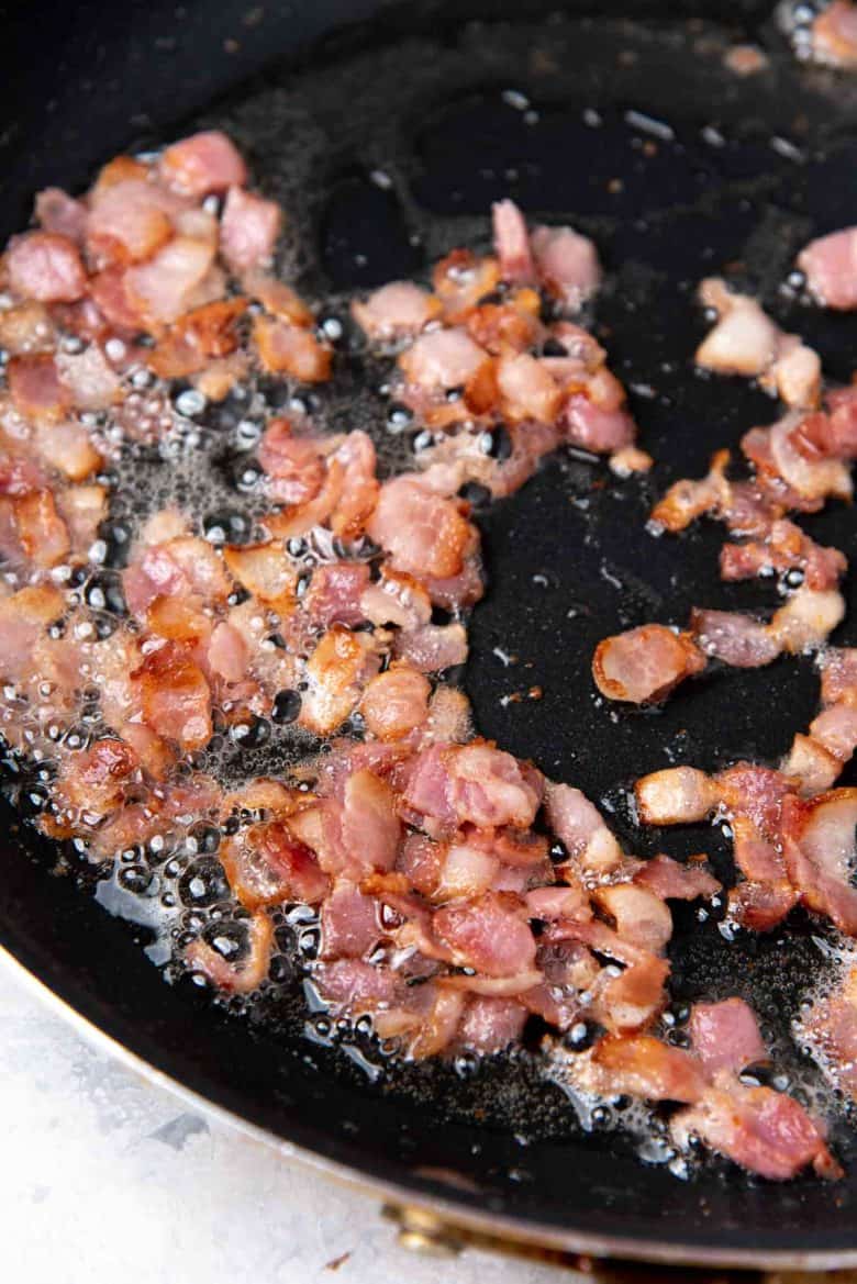 Close up picture of cut up bacon frying in a pan