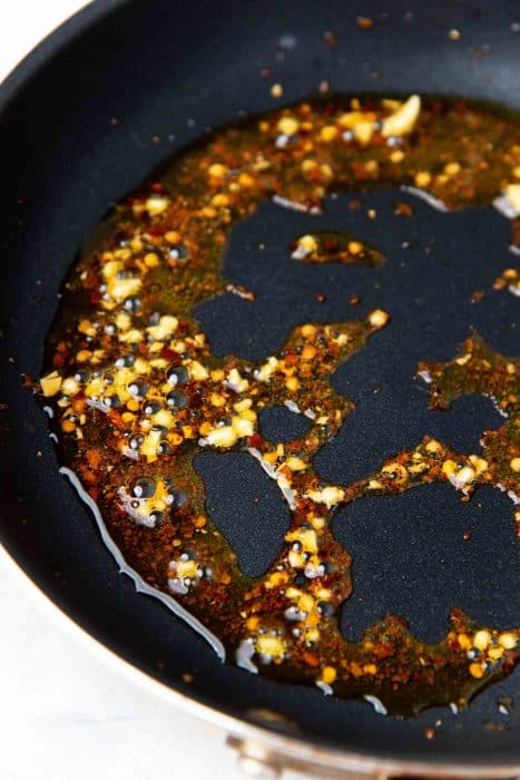A small frying pan with hot oil, garlic and chili flakes