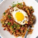 Breakfast fried rice served in a bowl with a chili garlic fried egg, bacon and roasted peanuts.