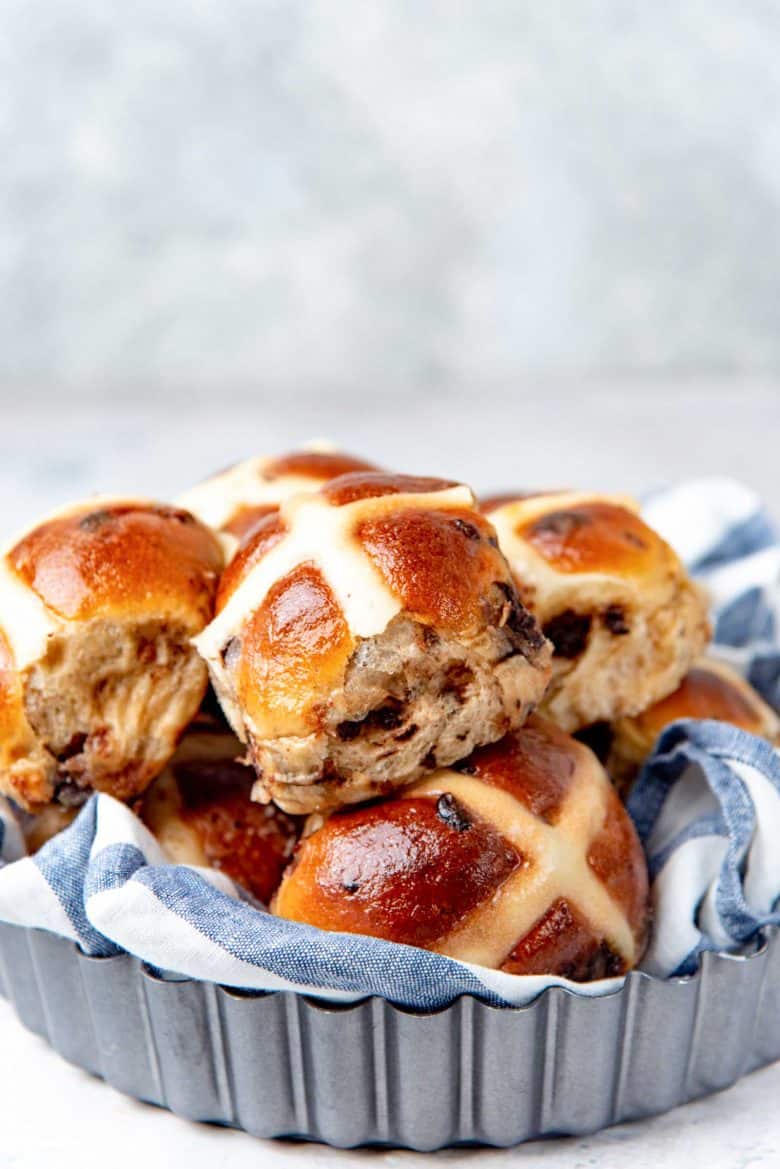 Chocolate chip hot cross buns stacked inside a cloth lined pan.