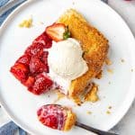 A rustic strawberry galette topped with fresh strawberries and a scoop of vanilla ice cream.