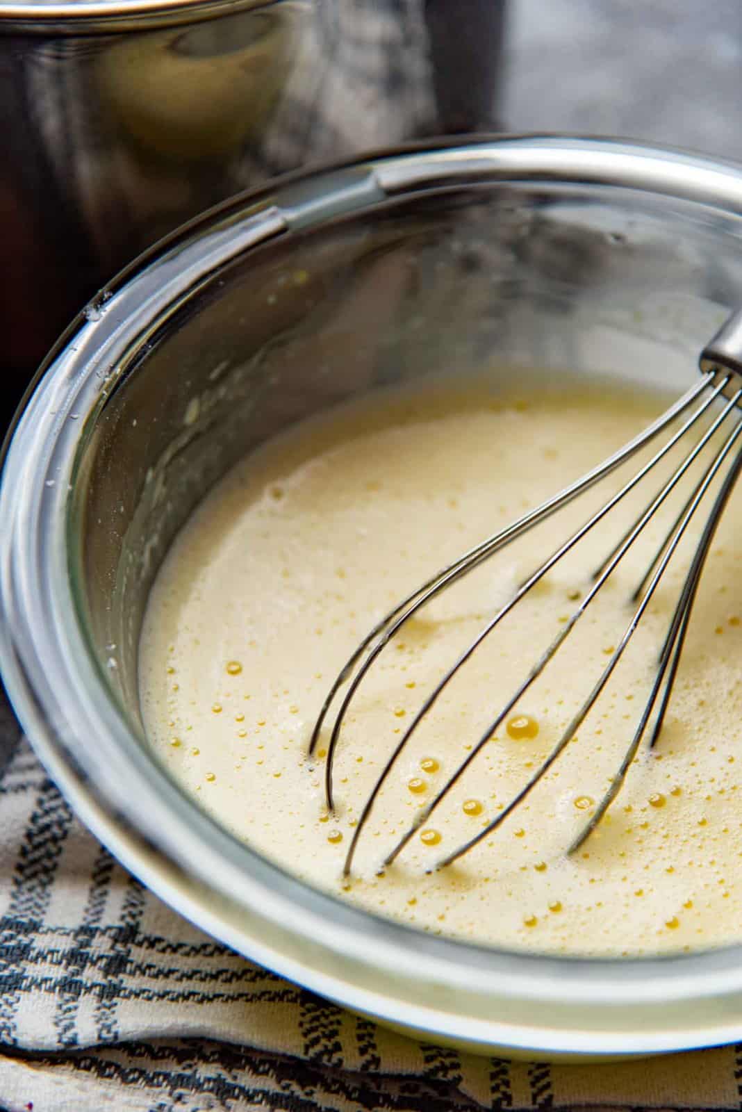 The egg mixture warmed up with milk (Tempering eggs) in a bowl with a whisk.