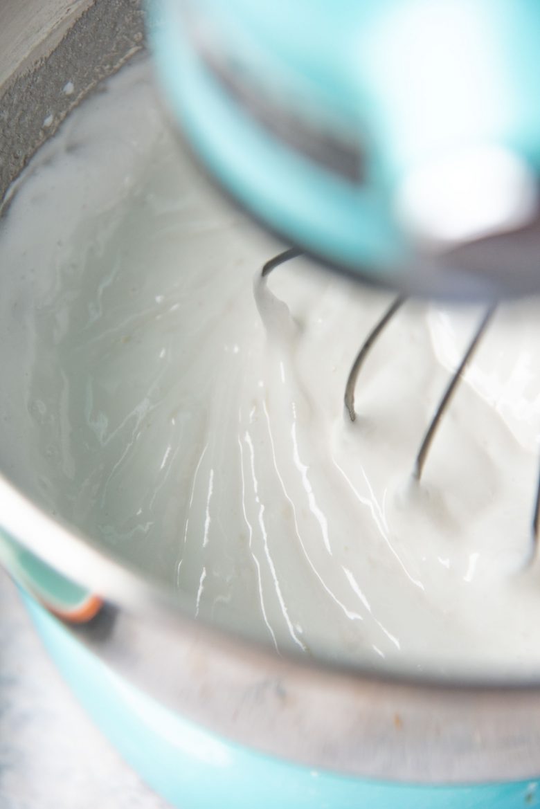 Egg white meringue base starting to form in the mixing bowl with the whisk attachment in the stand mixer.