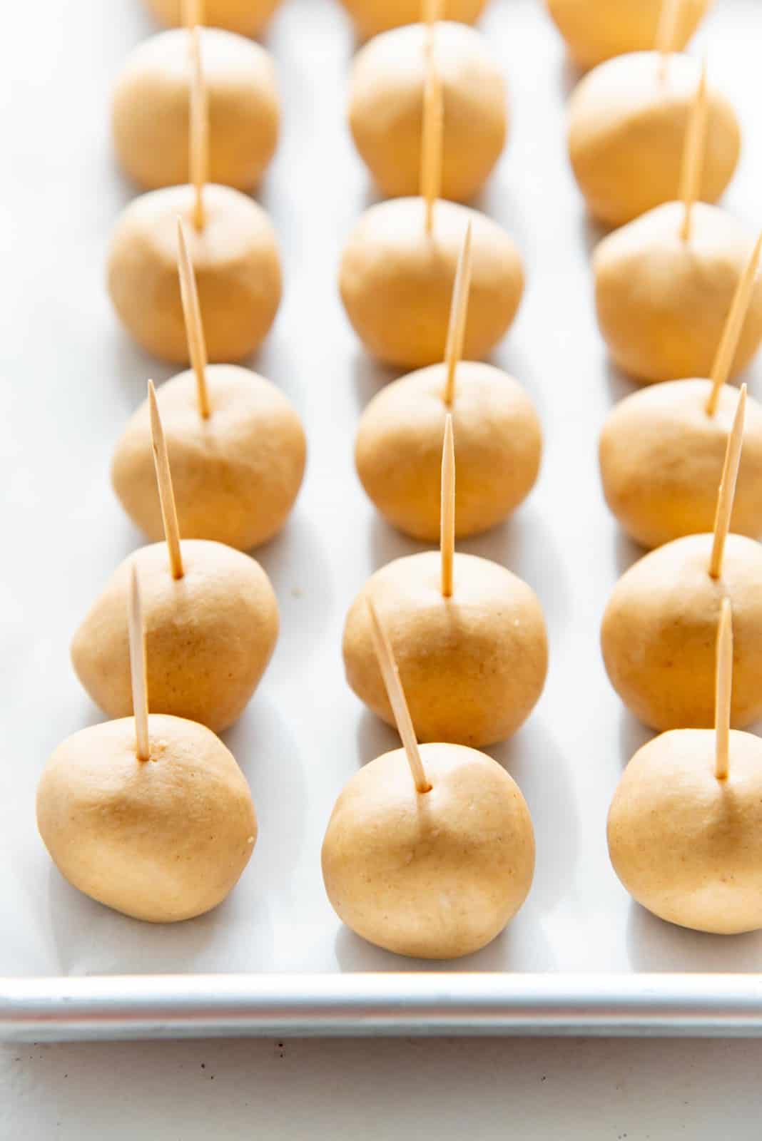 The peanut butter fudge balls on a tray with toothpicks attached, lined up on the baking tray ready to be chilled.
