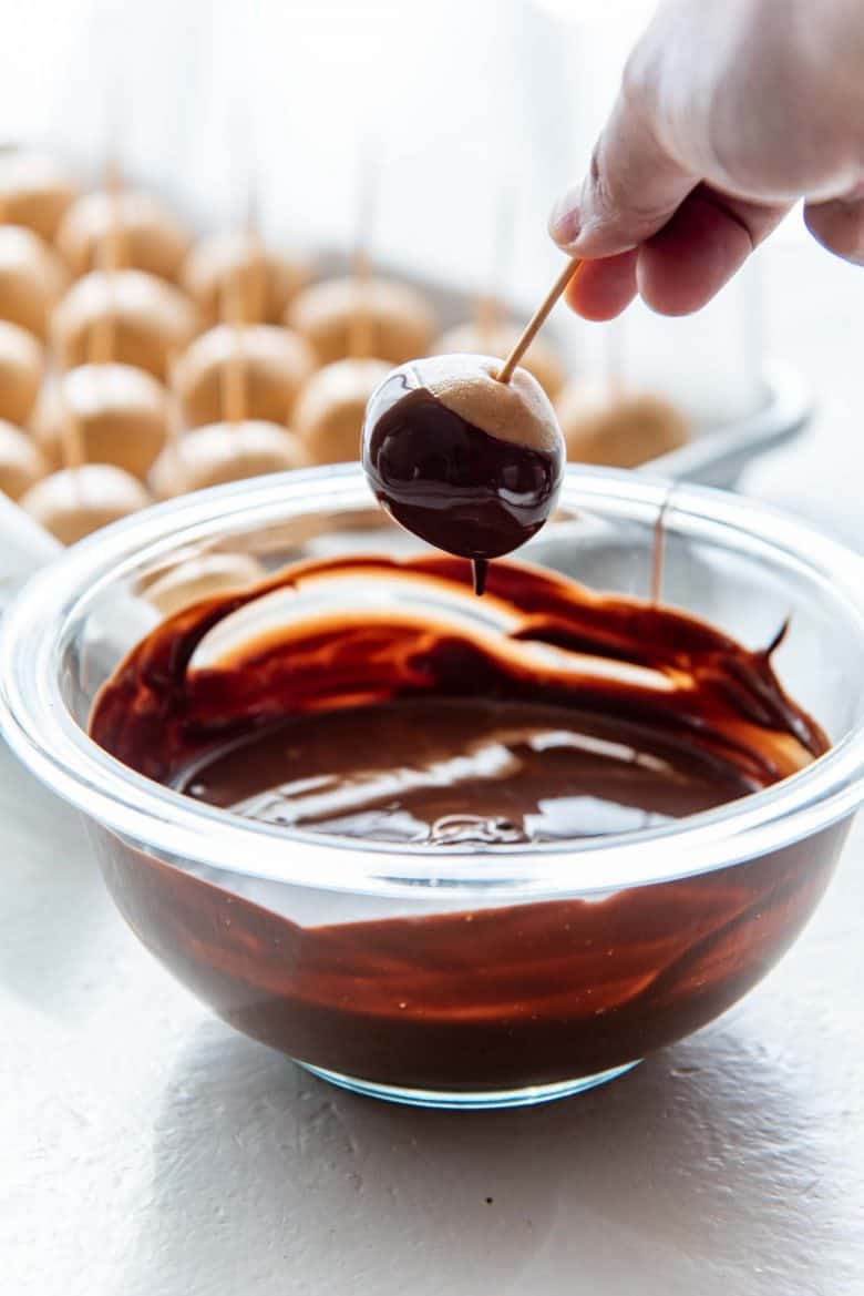 Peanut butter ball being dipped in melted chocolate, with the help of a toothpick attached to the peanut butter ball