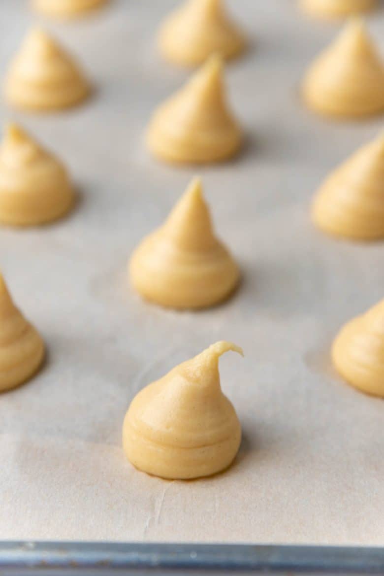 Piped choux pastry wth a long pointed tip on a parchment lined baking tray
