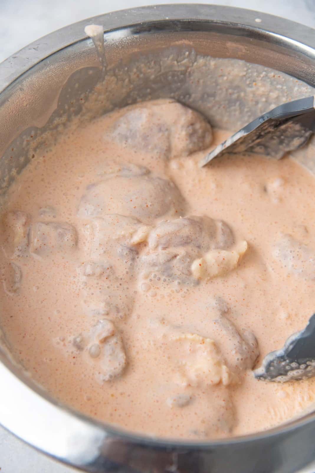 Chicken thighs marinating in a seasoned buttermilk mixture