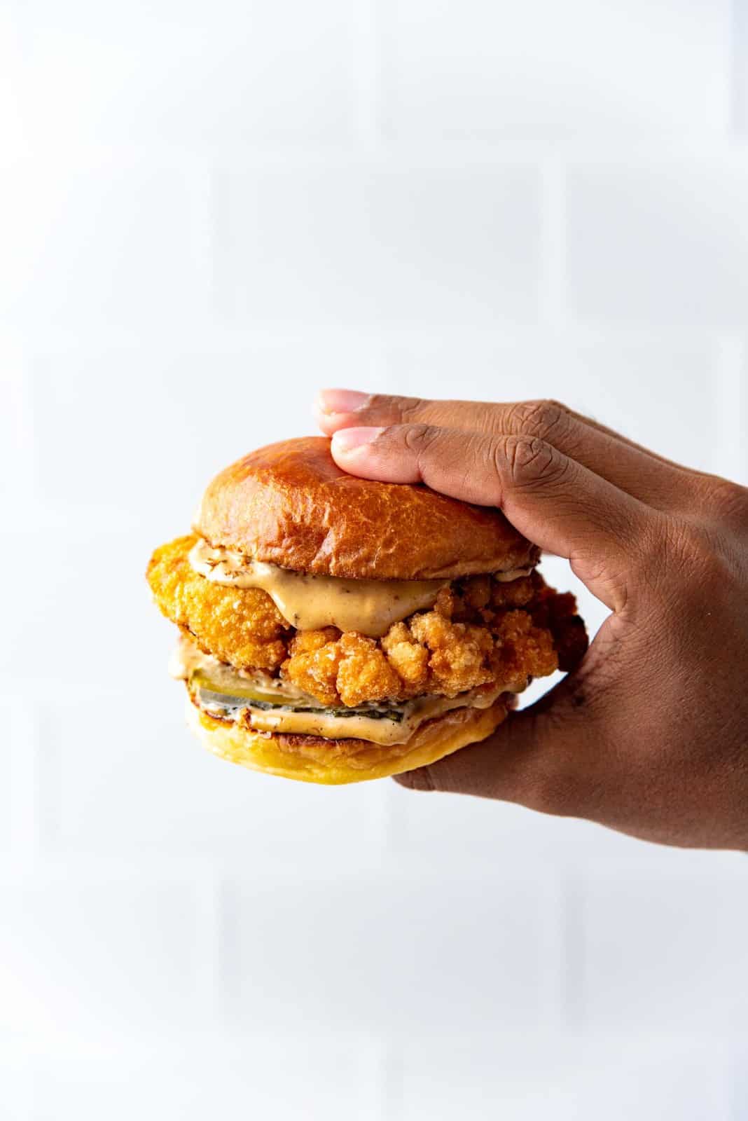 The chicken sandwich being held by a hand against a white background